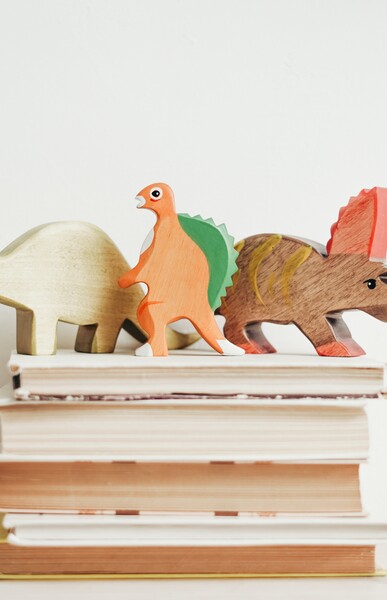 trois dinosaures en bois sur une pile de livres