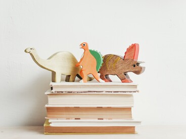 trois dinosaures en bois sur une pile de livres